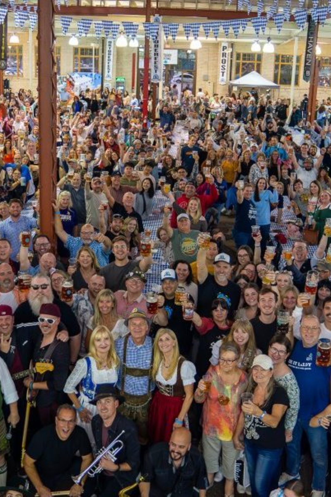 Multiple people outside, dressed in Oktoberfest attire, raising their beers